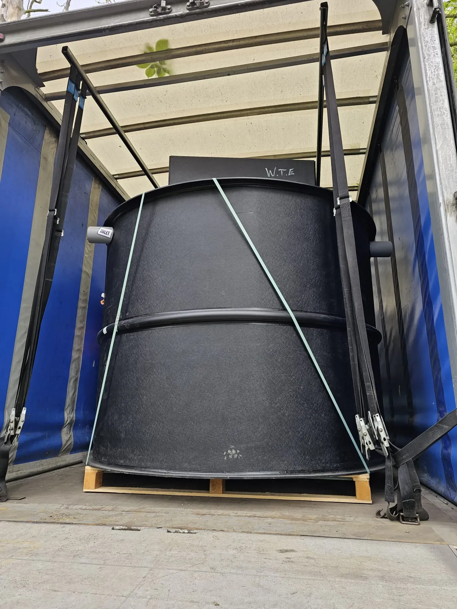 Large black sewage treatment plant or septic tank being transported in a lorry for installation.