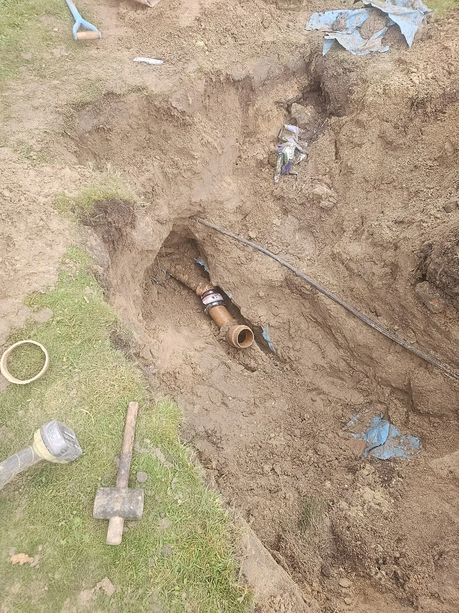 View of an open trench with a brown drainage pipe and coupling, showing drainage system installation or repair.