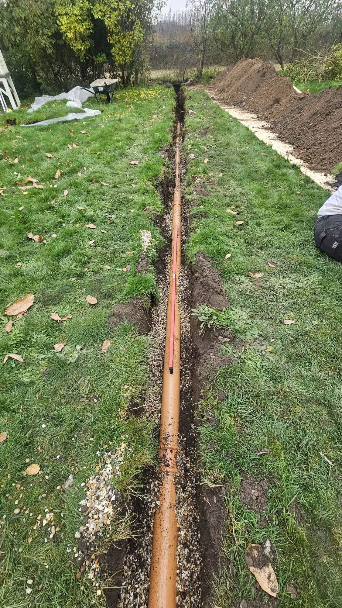 New drainage pipe being installed in a trench in a green garden area