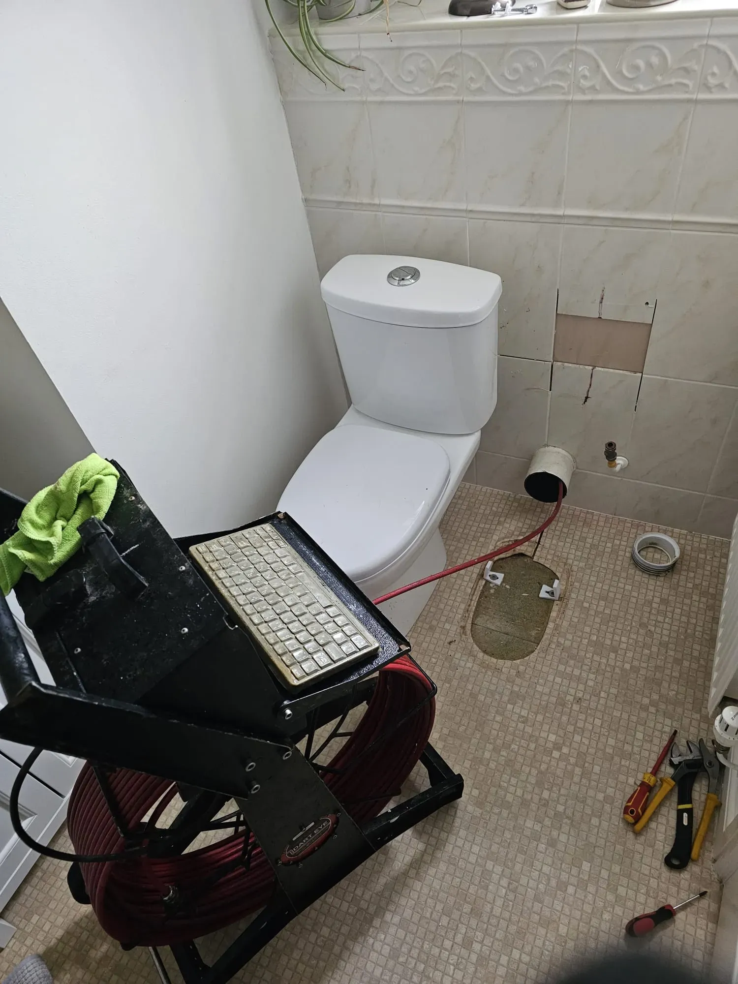 CCTV drain survey equipment being used to inspect pipes in a bathroom, with a camera cable going into a wall next to a toilet.
