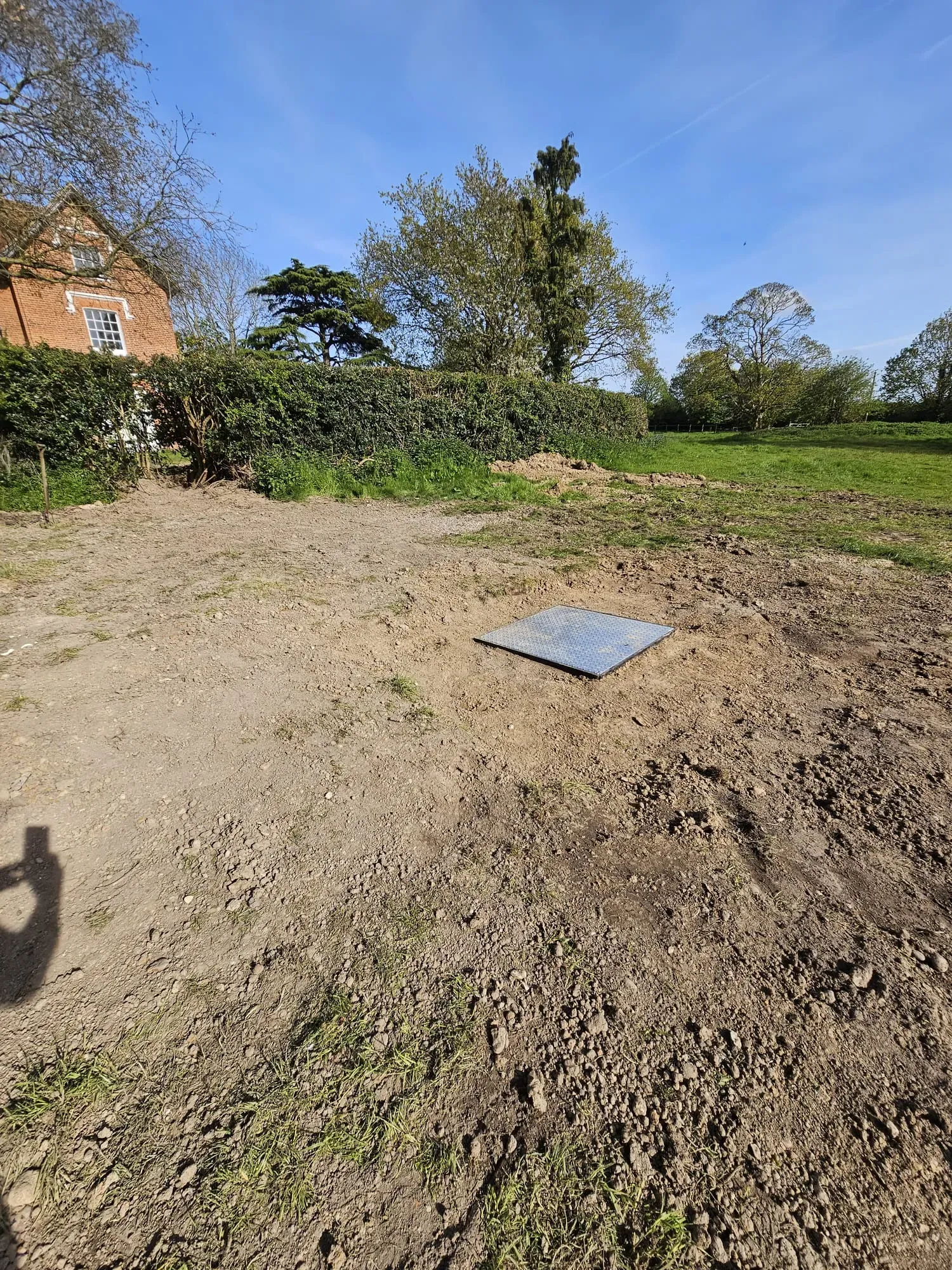 Metal access cover for an off-mains drainage system in a cleared garden.