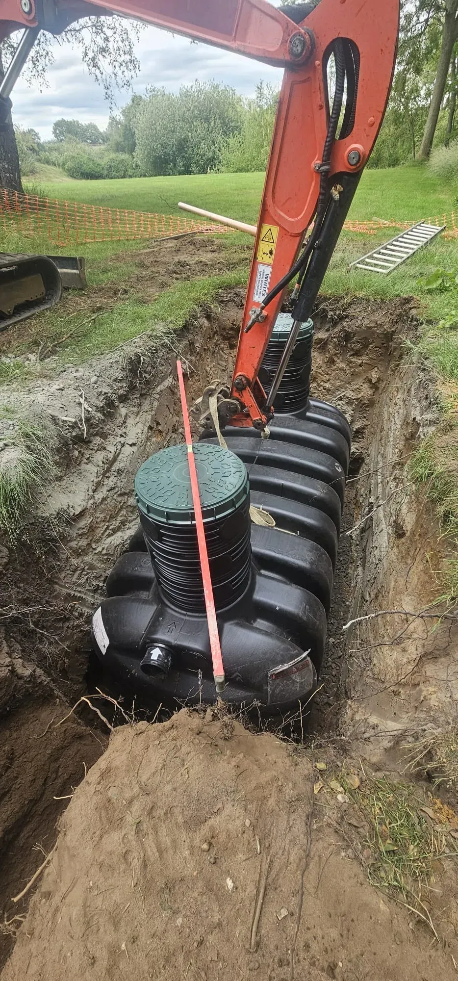 Professional installation of a new septic tank or sewage treatment plant by Eco Drain Solutions Ltd, using an excavator in a prepared trench.