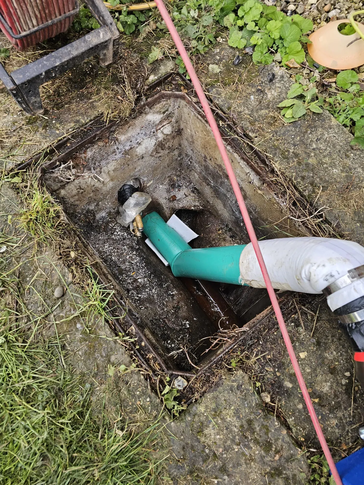 Specialist drainage equipment, including a green pipe and white flexible hose, inserted into an outdoor drain for unblocking or CCTV survey services.