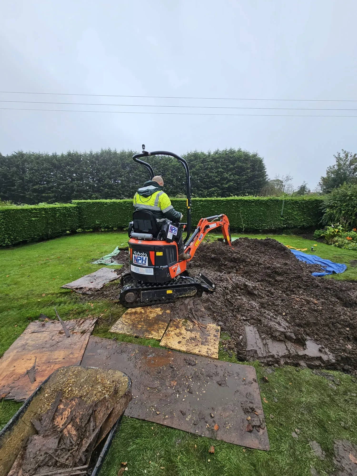 Mini excavator digging a trench in a garden for drainage or groundwork services